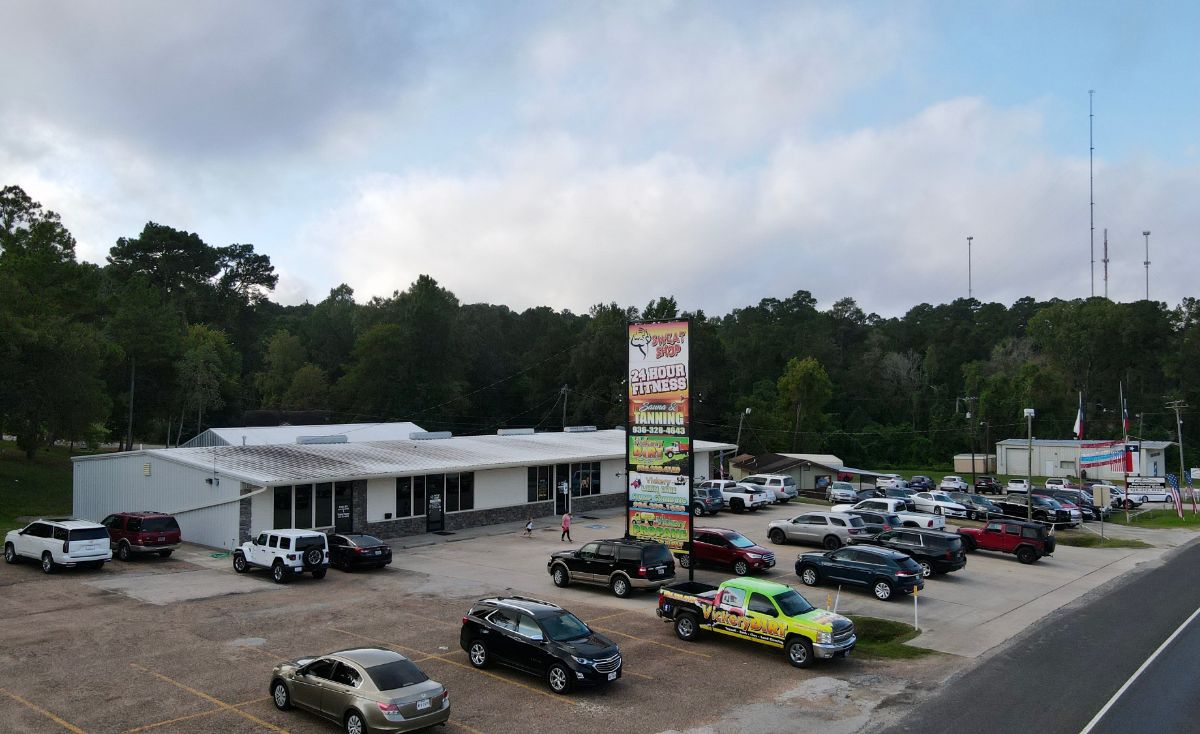 Vickery's Sweat Shop fitness center exterior with 24-hour access sign, surrounded by parked cars and greenery.