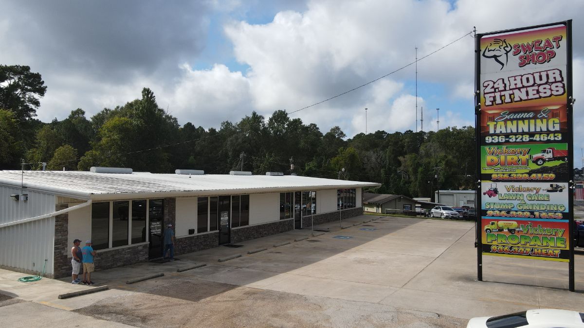 Vickery's Sweat Shop exterior view featuring gym building, fitness center signage, and two individuals in front, promoting 24-hour fitness and wellness services.