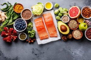 Colorful array of nutritious foods including salmon fillets, fruits, vegetables, nuts, and seeds, emphasizing healthy eating for fitness and nutrition.